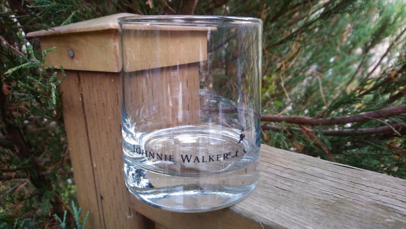K&ouml;nnte beinhalten: Ein klares Glas mit der Aufschrift "Johnnie Walker" auf dem Boden. Das Glas steht auf einer Holzoberfl&auml;che.