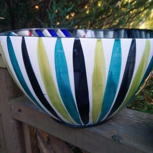 以下が含まれることがあります： 黒、緑、青のストライプが入った大きな白いセラミックボウル。ボウルは木製の表面の上に置かれています。