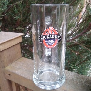 May include: A clear glass beer stein with a handle. The stein features a red, white and black logo that says "Rickard's Red".