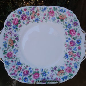 Puede incluir: Un plato de servir de cerámica blanca con un borde dorado y un patrón floral en tonos de rosa, azul y amarillo.