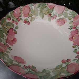May include: A large white ceramic serving bowl with a pink and green floral design. The bowl has a scalloped edge and is ideal for serving salads, pasta, or fruit.