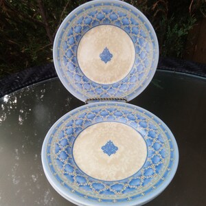 May include: Two blue and white ceramic plates with a decorative pattern. The plates have a cream-colored center with a blue and gold design.