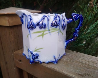 Jarra de leche de porcelana marcada con el número 748, decoración floral azul en relieve, detalles dorados, decoración verde, borde festoneado, mango azul crema y dorado