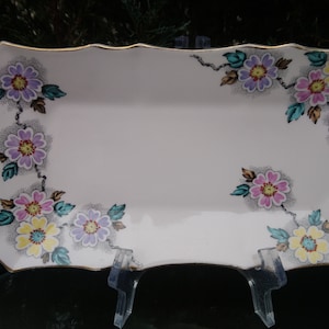 Peut inclure: Un plat de service rectangulaire blanc avec un bord doré et un motif floral. Les fleurs sont roses, violettes, jaunes et vertes.