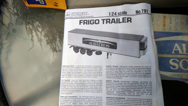 May include: A black and white diagram of a Frigo Trailer model, scale 1:24, with the name "ALBATROS" on the side. The model has six wheels and is a refrigerated trailer. The text "FRIGO TRAILER" is at the top.