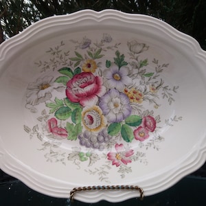 May include: White oval serving bowl with a floral design featuring pink, purple, and yellow flowers. The bowl has a scalloped edge.
