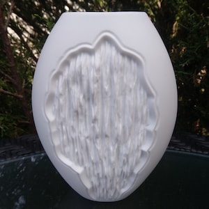 May include: White ceramic vase with a textured, wood-like design. The vase is oval shaped and has a wide opening.