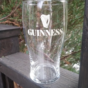 Puede incluir: Un vaso de pinta de vidrio transparente con el logotipo de Guinness y un dise&ntilde;o de arpa. El vaso est&aacute; vac&iacute;o y se encuentra sobre una superficie de madera.