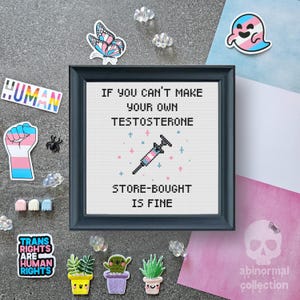 May include: A cross-stitch embroidery with a black frame and a white background. The embroidery features a syringe with a pink and blue color scheme, and the text "If you can't make your own testosterone, store-bought is fine".