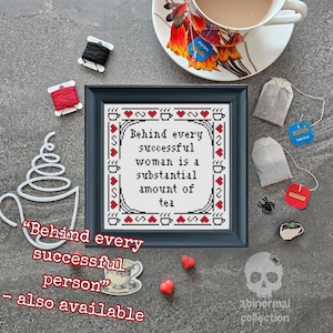 Peut inclure: Un motif de point de croix encadré avec un cadre noir et un tissu blanc. Le motif de point de croix présente des cœurs rouges et le texte "Behind every successful woman is a substantial amount of tea".