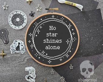 May include: Black and white embroidery hoop with the text "No star shines alone" surrounded by stars. The hoop is on a gray background with other black and white decorations.