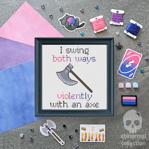 Pode incluir: Um design de ponto cruz enquadrado com o texto "I swing both ways violently with an axe". O design apresenta um machado cinza com um cabo marrom. O fundo é branco. A moldura é cinza escuro.