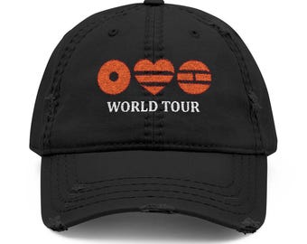 May include: Black distressed baseball cap with an orange graphic of a circle, heart, and a segmented circle above the words "WORLD TOUR" in white. The cap has a curved brim and a distressed look.