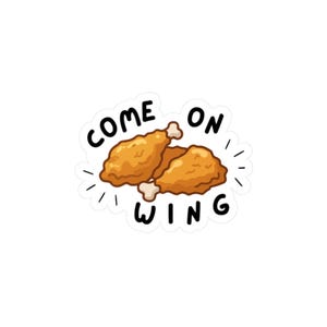 Peut inclure: Un autocollant représentant deux ailes de poulet frites de dessin animé avec le texte "COME ON WING" en noir, souligné de blanc. Les ailes sont brun doré sur fond blanc.