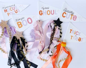 Puede incluir: Un conjunto de seis banderines temáticos de Halloween con varias frases, que incluyen "Hocus Pocus", "Love you BOO", "My best GHOUL", "Spooky CUTE" y "TRICK or TREAT". Los banderines están decorados con estrellas y lunares. También hay cinco varitas con cintas y estrellas de brillantina.