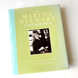 May include: The Martha Stewart Cookbook with a light green cover and a photo of Martha Stewart. The book's title is in large, bold, white letters. The subtitle reads "Collected Recipes for Every Day."