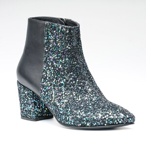 May include: A black ankle boot with a glittery, iridescent finish. The boot features a black leather back panel and a chunky, block heel. The boot has a pointed toe and a zipper closure. The overall style is fashionable and eye-catching.