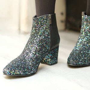 May include: Glitter ankle boots with a pointed toe and block heel. The boots are covered in iridescent glitter, with a black leather back and zipper. The heels are approximately 3 inches high.