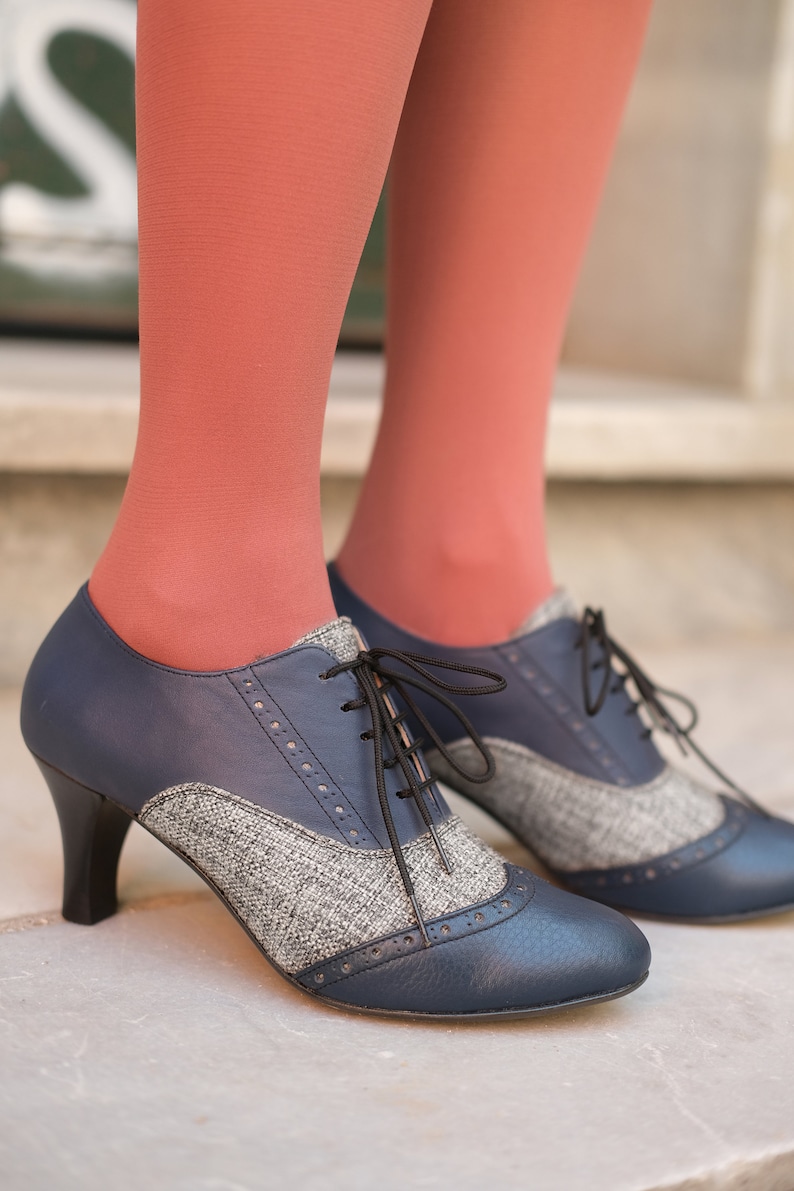 May include: A pair of blue and grey tweed heeled shoes with black laces. The shoes have a pointed toe and a small heel.