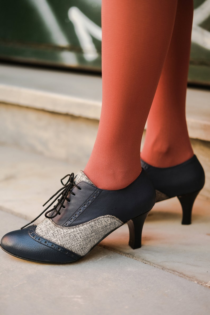 May include: A pair of black and grey heeled shoes with a lace-up fastening. The shoes feature a tweed-like fabric on the upper part and a smooth leather toe.