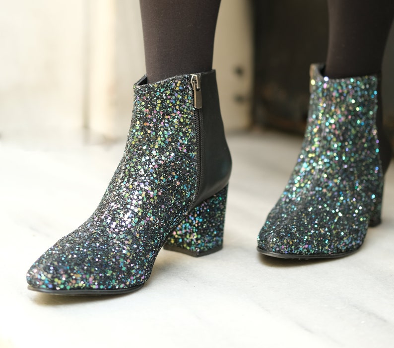 May include: Glitter ankle boots with a pointed toe and block heel. The boots are covered in iridescent glitter, with a black leather back and zipper. The heels are approximately 3 inches high.