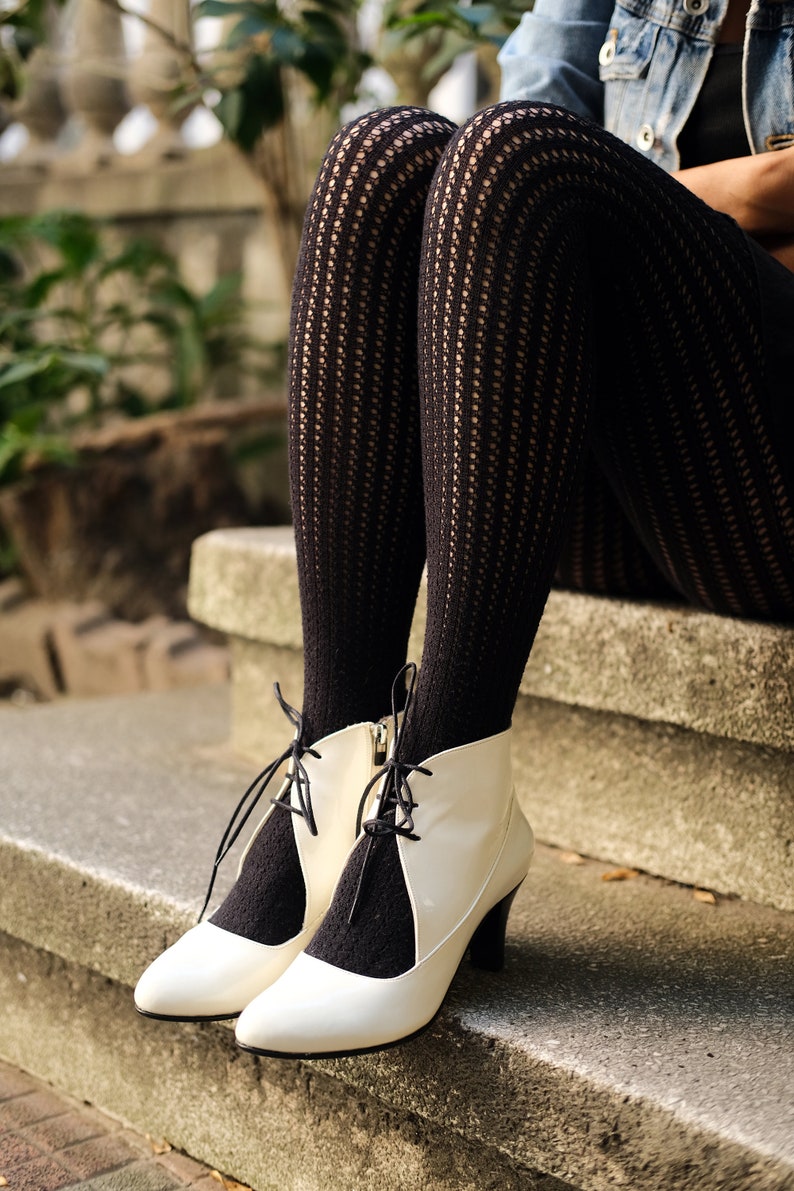May include: White heeled ankle boots with black lace-up detailing and black patterned tights.