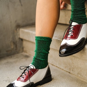 May include: A pair of black and white leather oxfords with red accents. The shoes are worn with green sparkly socks.