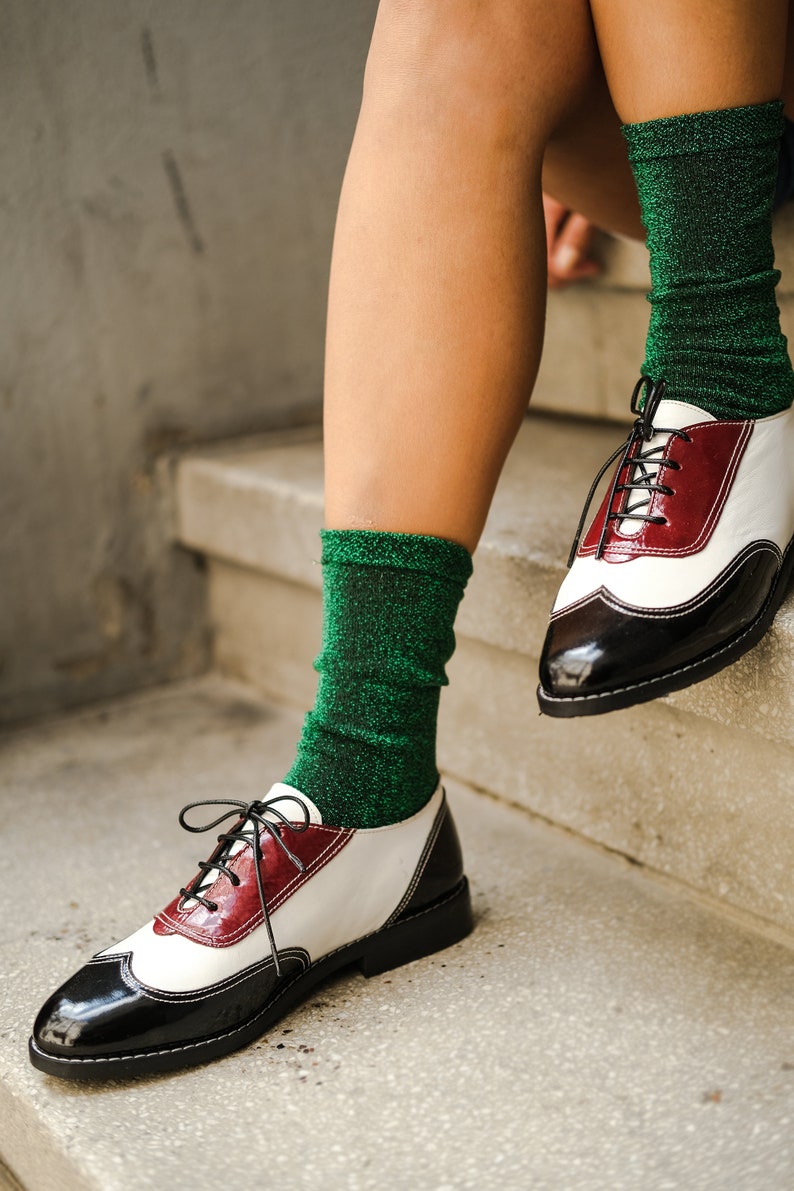 May include: A pair of black and white leather oxfords with red accents. The shoes are worn with green sparkly socks.