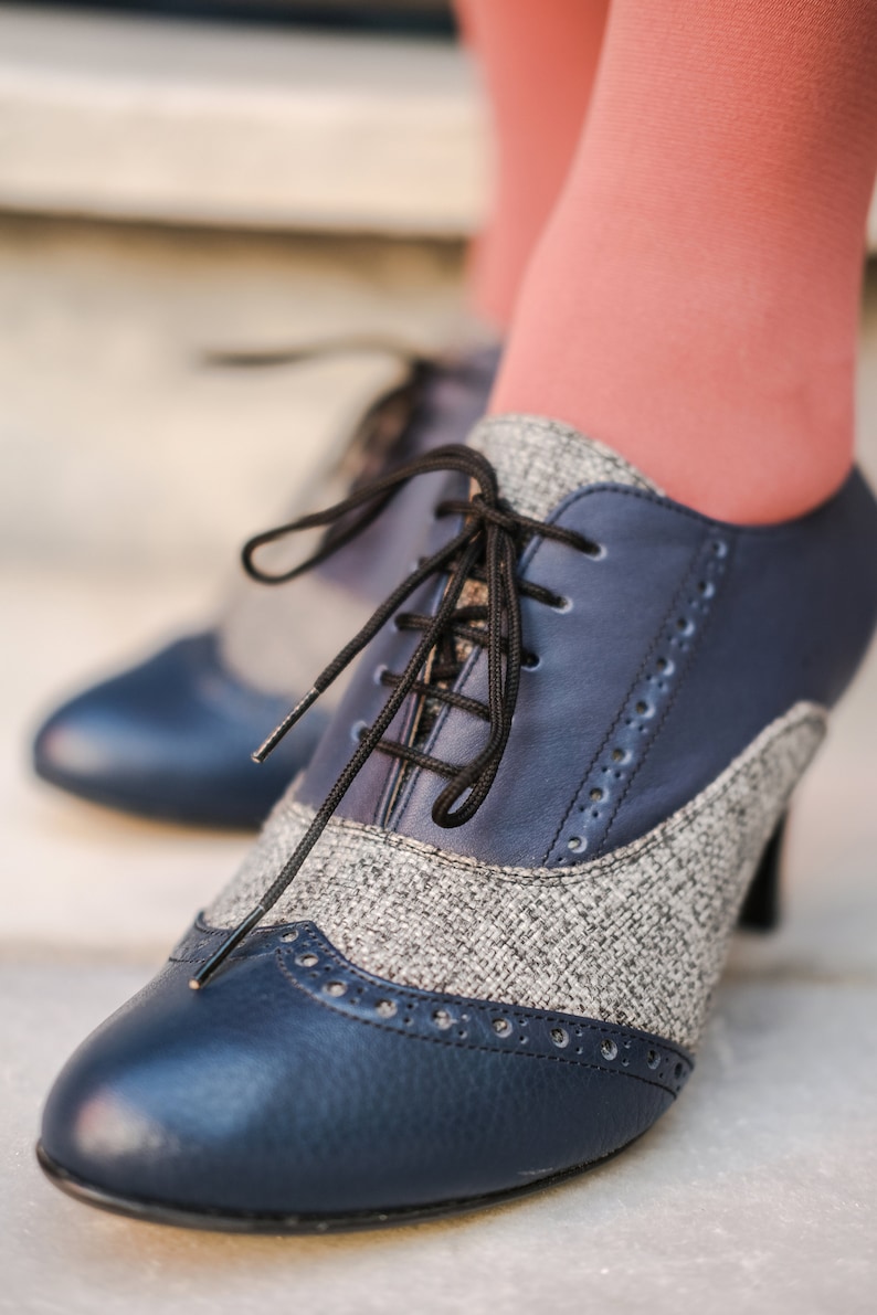 May include: Blue and grey tweed heeled shoes with black laces. The shoes have a pointed toe and a decorative stitch pattern.