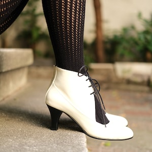 May include: White leather ankle boots with black laces. The boots have a low heel and are worn with black fishnet stockings.