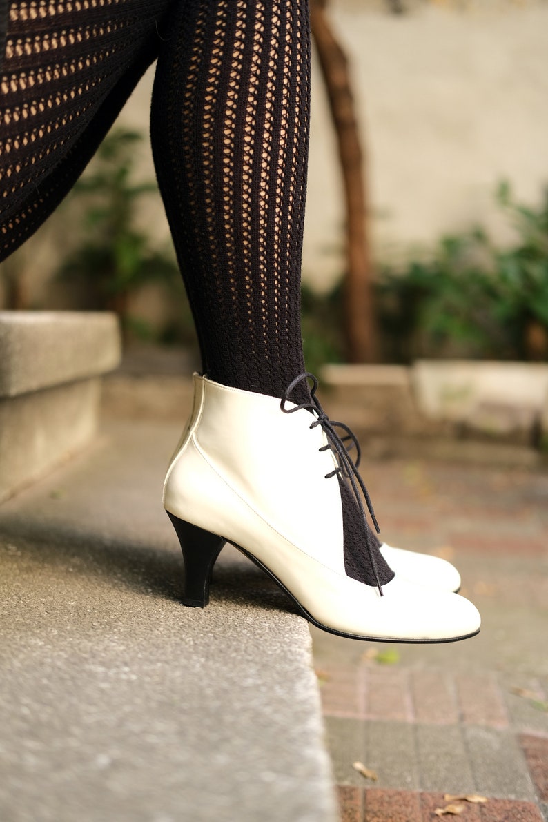 May include: White leather ankle boots with black laces. The boots have a low heel and are worn with black fishnet stockings.