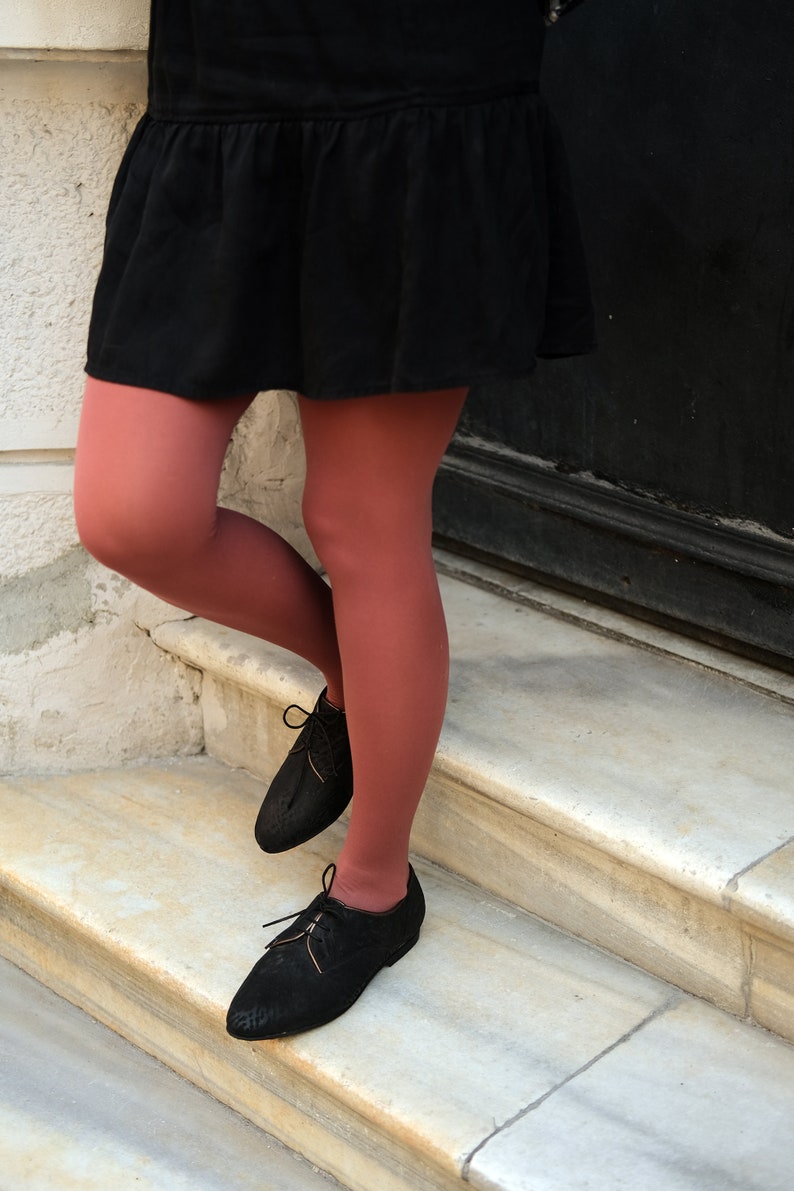 May include: A person wearing a black skirt and red tights, standing on a set of white marble stairs. They are wearing black lace-up shoes.