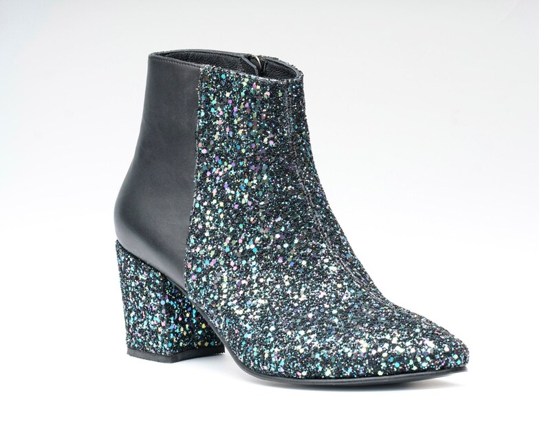 May include: A black ankle boot with a glittery, iridescent finish. The boot features a black leather back panel and a chunky, block heel. The boot has a pointed toe and a zipper closure. The overall style is fashionable and eye-catching.