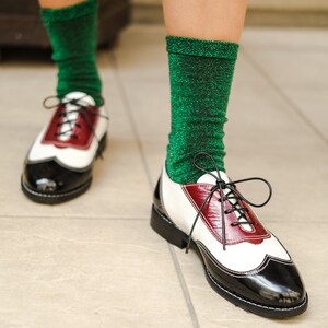 May include: A pair of white and black leather shoes with red accents. The shoes have laces and are worn with green sparkly socks.
