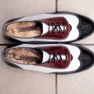 May include: A pair of black and white leather shoes with burgundy accents. The shoes have a lace-up closure and a rounded toe.