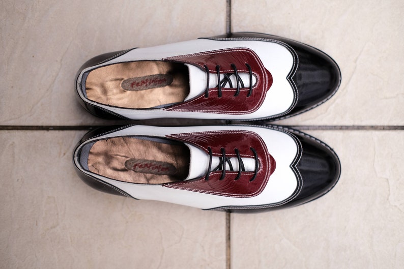 May include: A pair of black and white leather shoes with burgundy accents. The shoes have a lace-up closure and a rounded toe.
