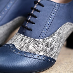 May include: A pair of blue and grey leather shoes with a brogue design. The shoes have a lace-up fastening and a chunky heel.