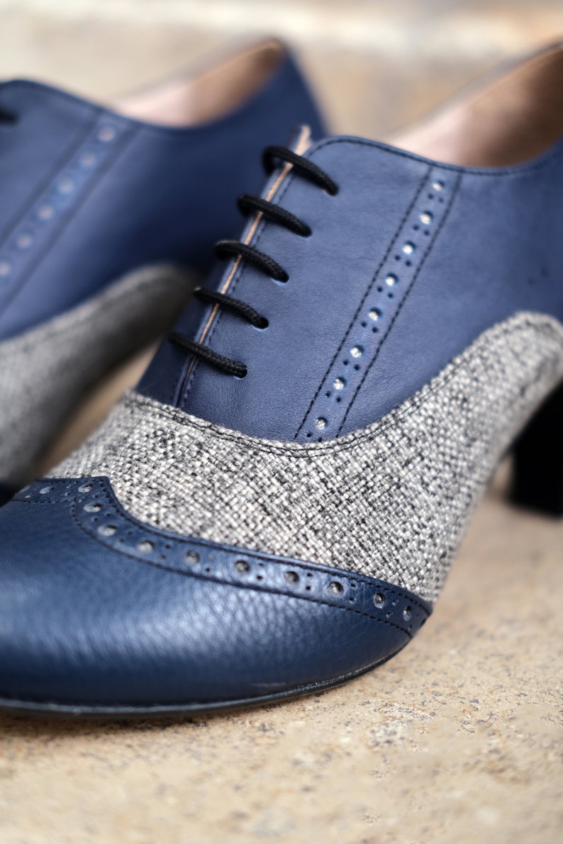 May include: A pair of blue and grey leather shoes with a brogue design. The shoes have a lace-up fastening and a chunky heel.