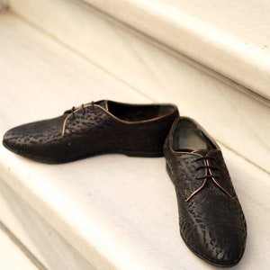 May include: A pair of black leather lace-up shoes with a subtle embossed pattern. The shoes have a brown trim around the edges.