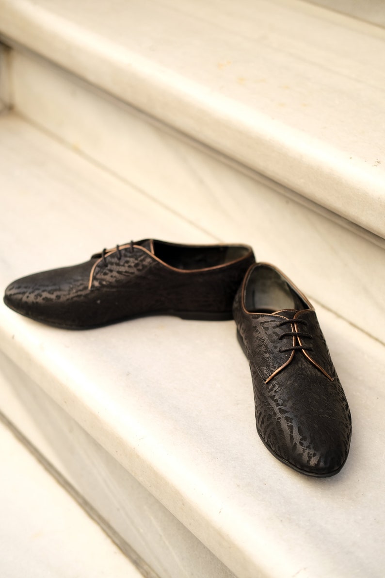 May include: A pair of black leather lace-up shoes with a subtle embossed pattern. The shoes have a brown trim around the edges.