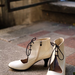 May include: A pair of white heeled shoes with black laces. The shoes have a pointed toe and a cut-out design on the side.