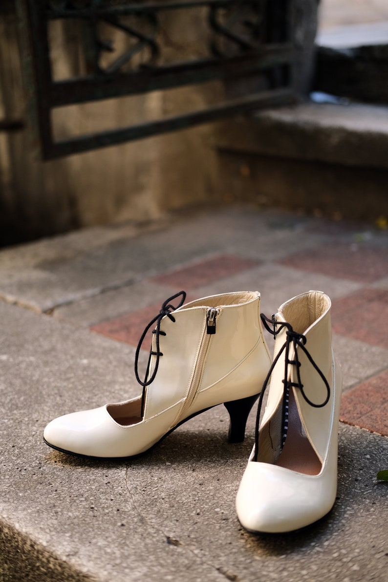 May include: A pair of white heeled shoes with black laces. The shoes have a pointed toe and a cut-out design on the side.