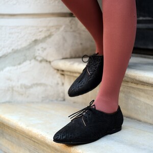 May include: A pair of black leather oxfords with laces. The shoes have a textured pattern and are worn with rust-coloured tights.