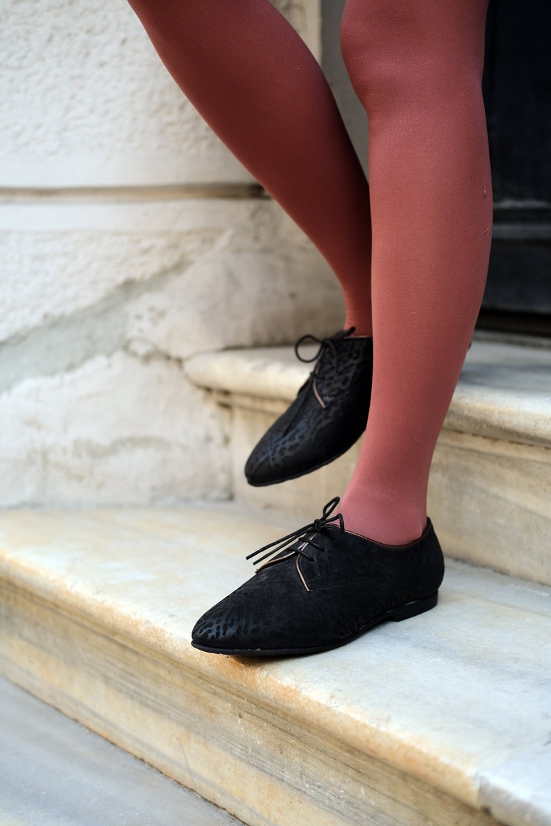 May include: A pair of black leather oxfords with laces. The shoes have a textured pattern and are worn with rust-coloured tights.