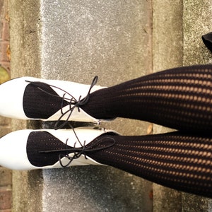 May include: A pair of white shoes with black lace-up detailing and black fishnet stockings.