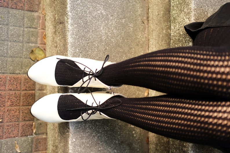 May include: A pair of white shoes with black lace-up detailing and black fishnet stockings.