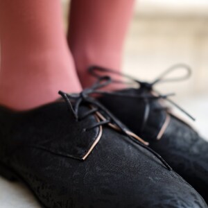 May include: Black leather lace-up shoes with a subtle pattern. The shoes have a rounded toe and a low heel.