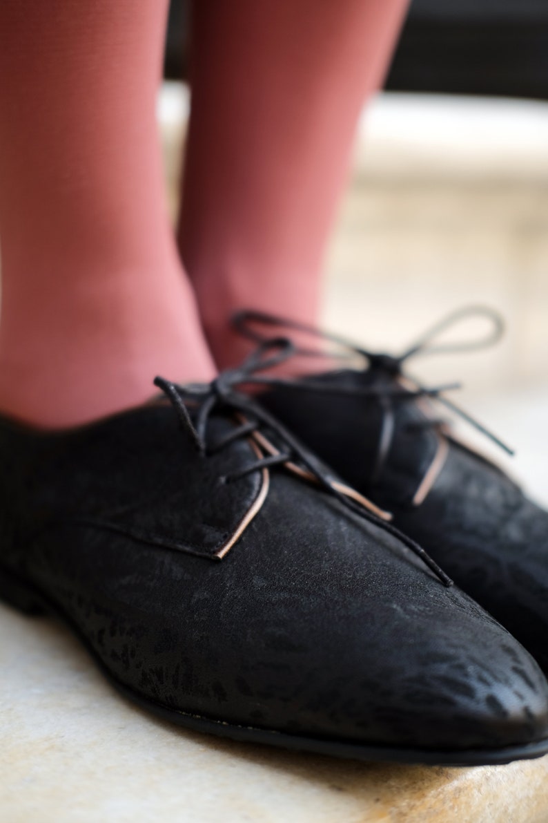 May include: Black leather lace-up shoes with a subtle pattern. The shoes have a rounded toe and a low heel.
