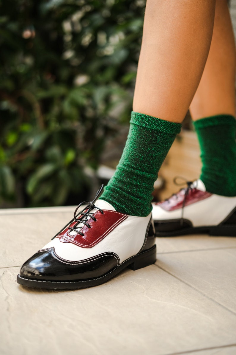 May include: Black and white leather oxford shoes with a red accent and green glitter socks.