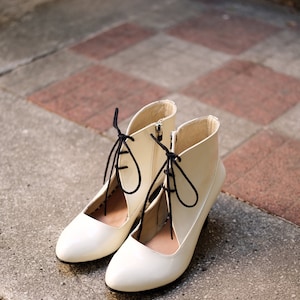 May include: A pair of white ankle boots with black laces. The boots have a pointed toe and a low heel.
